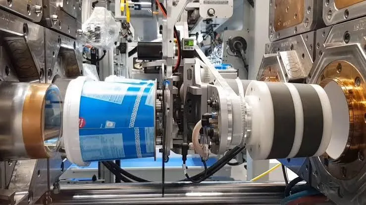 In-mould labelling machine placing a printed label on a plastic tub